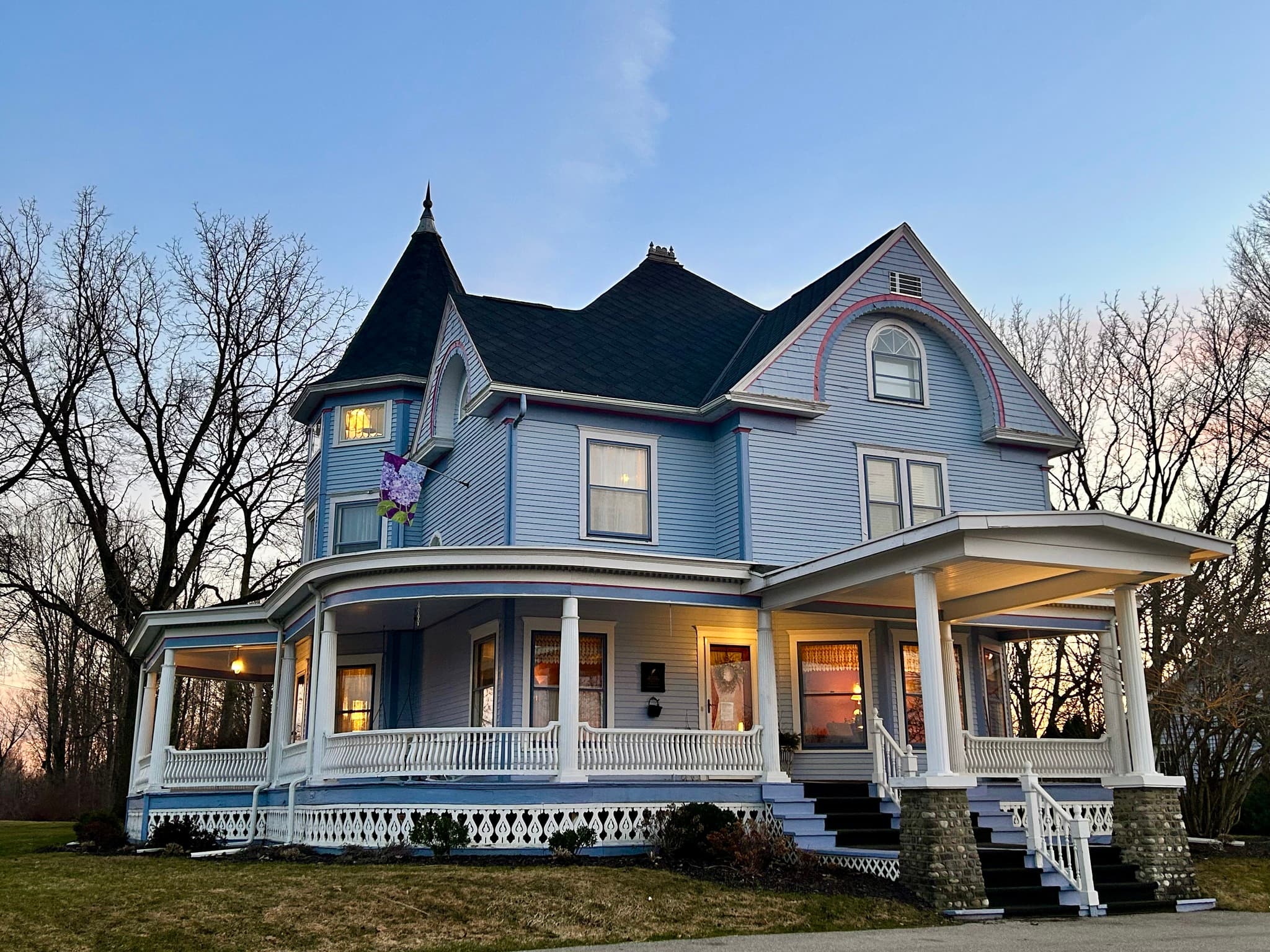 A large light blue Victorian-style house with a wraparound porch and an American flag. A large light blue Victorian-style house with a wraparound porch and an American flag.
