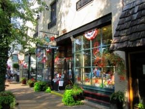 A quaint storefront with large windows adorned with flowers and decorative elements, set on a tree-lined street.