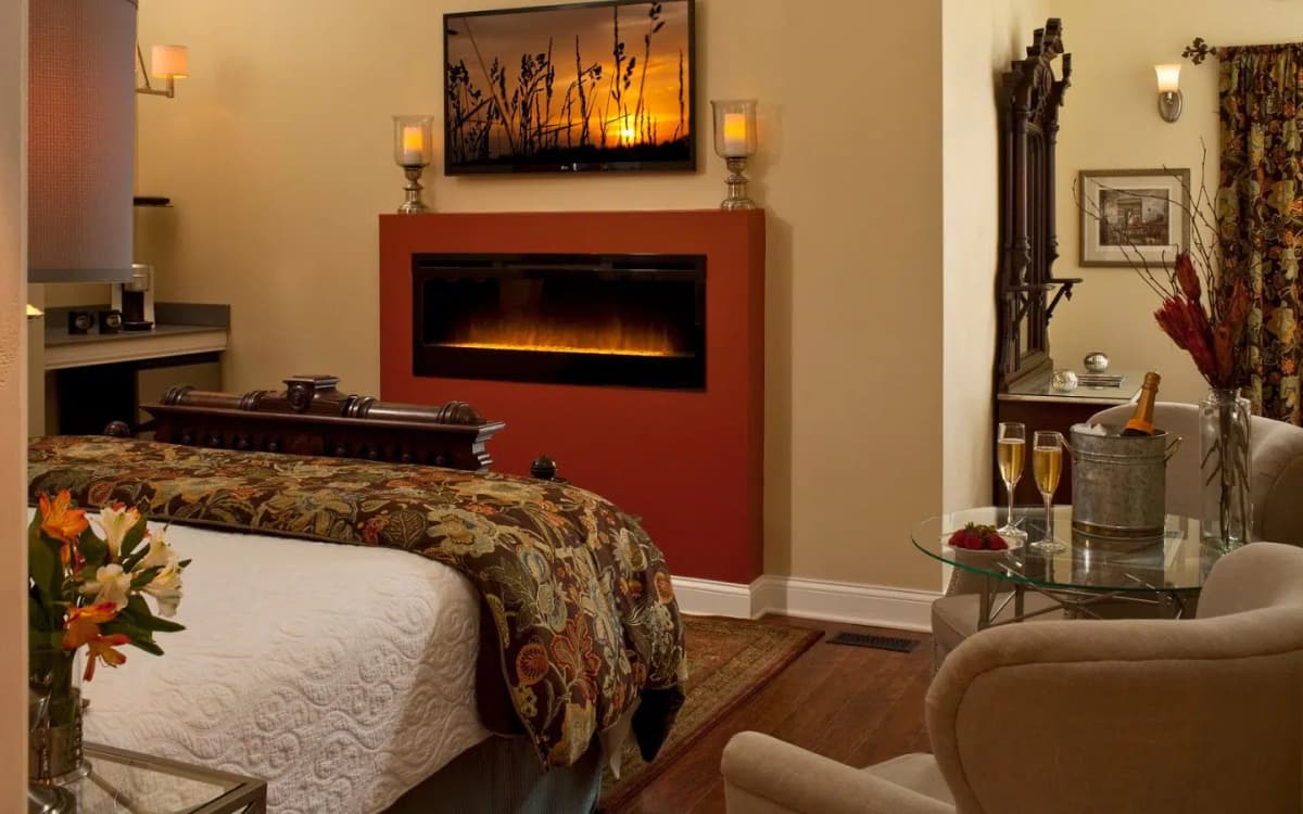 Camelot guest room with linear fireplace, king-size bed, and flat screen TV in warm earth tones