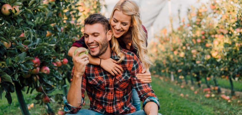 A romantic couple wearing flannels and jeans hugging in an apple orchard.