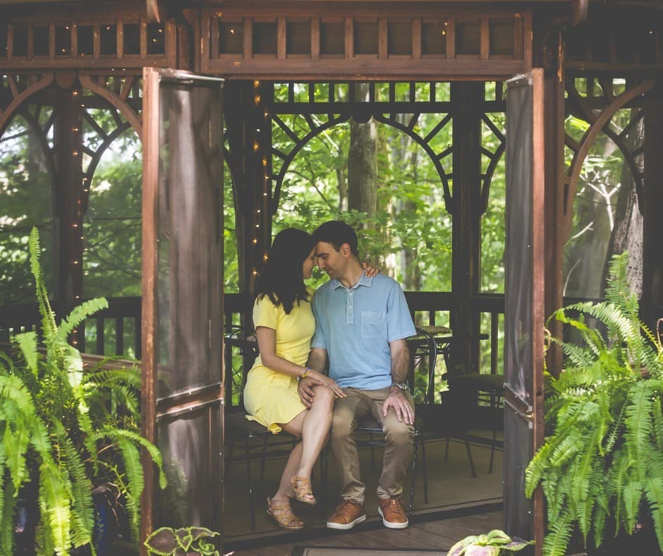 A spring couple embracing for a kiss under the trellis dusted with snow, while the woman holds white and purple flowers.
