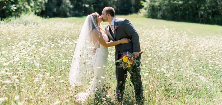 spring bridal couple kissing in meadow while groom holds vibrant flower bouquet
