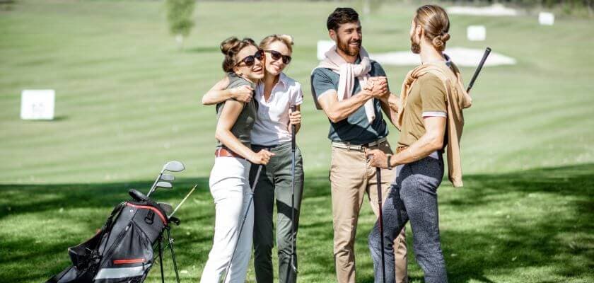 two women hugging and two men shaking hands while all hold golf clubs while on golf course