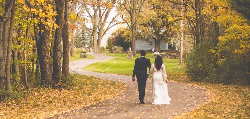 An autumn bridal couple walking the driveway toward Castle in the Country while surrounded by golden autumn foliage.