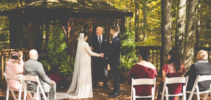 Late spring bridal couple during a micro wedding ceremony by the gazebo with guests.