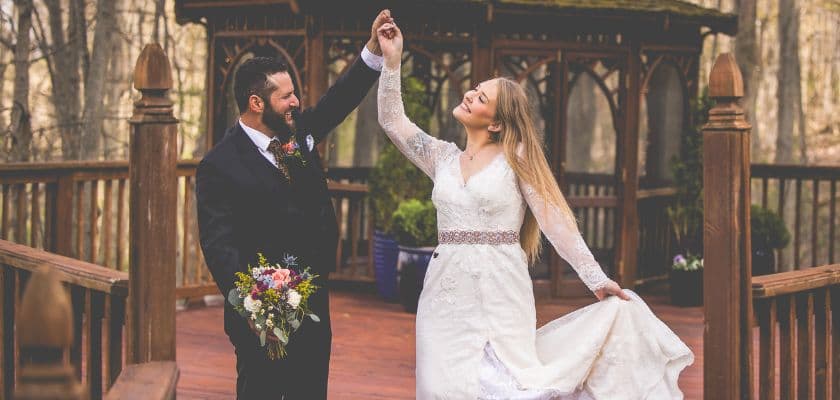 smiling autumn bridal couple dancing near the gazebo, the groom holds the bouquet with one hand and twirls the bride with the other