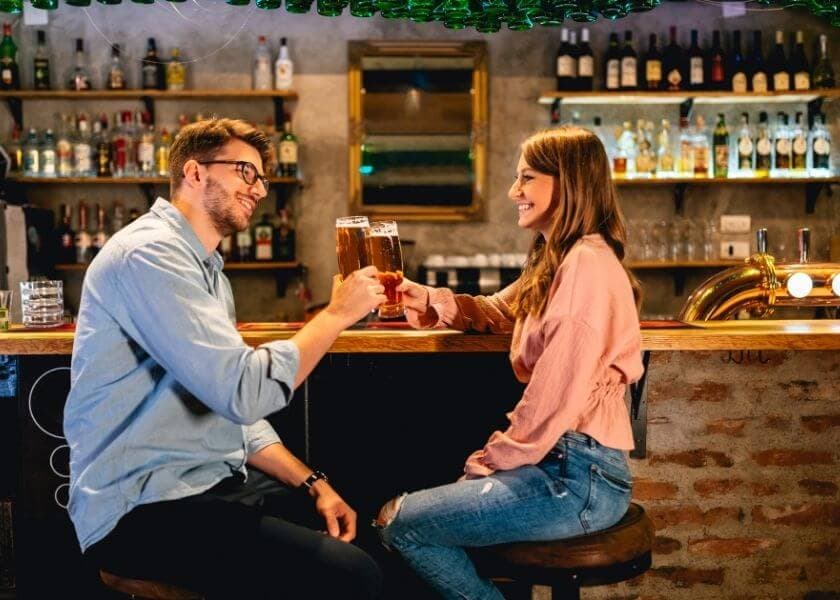 smiling romantic couple toasting pints of beer while seated at the bar of a brew pub smiling romantic couple toasting pints of beer while seated at the bar of a brew pub