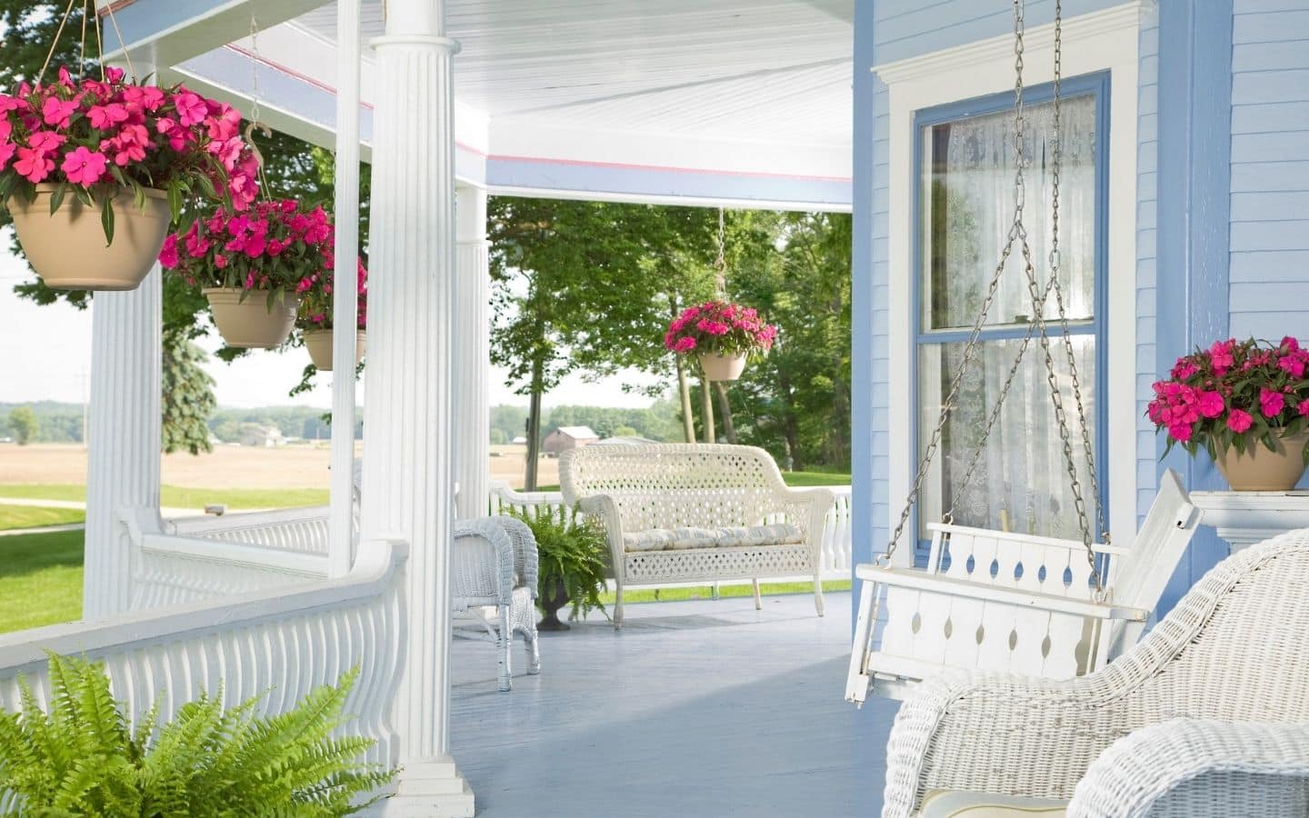 Front porch of the Inn with white trim, blue siding, wicker furniture and hanging baskets of red flowers