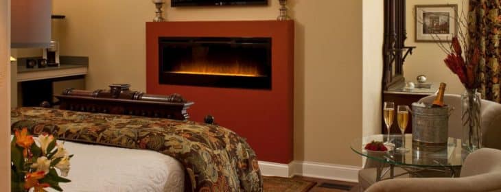 Camelot guest room with linear fireplace, king-size bed, and flat screen TV in warm earth tones