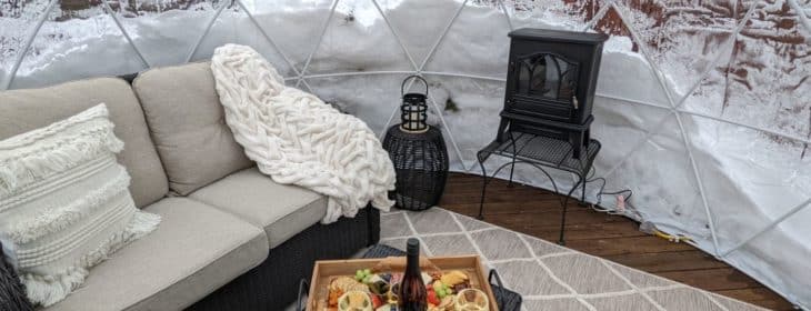 ozy loveseat, fire stove, charcuterie board and wine in the outdoor igloo during the winter.