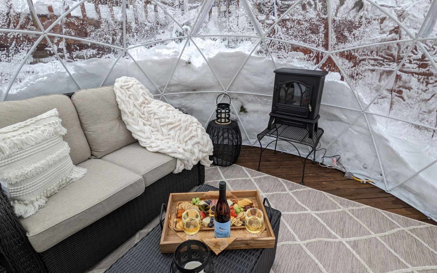 ozy loveseat, fire stove, charcuterie board and wine in the outdoor igloo during the winter.