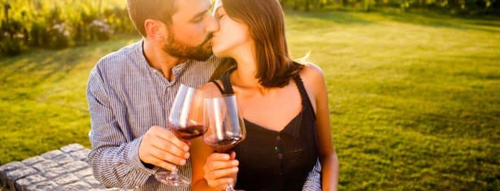 A couple is kissing while wine-tasting outside
