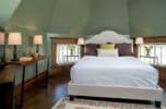 Room with a queen size bed with two widows and lamps on each side eight sided turret ceiling.