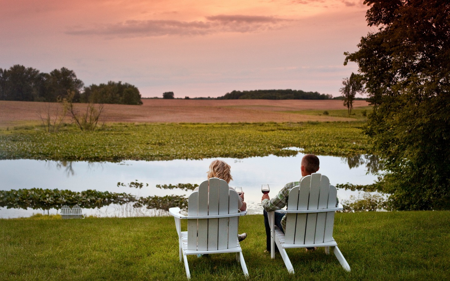 couple sitting on lawn chairs with wine overlooking the pond