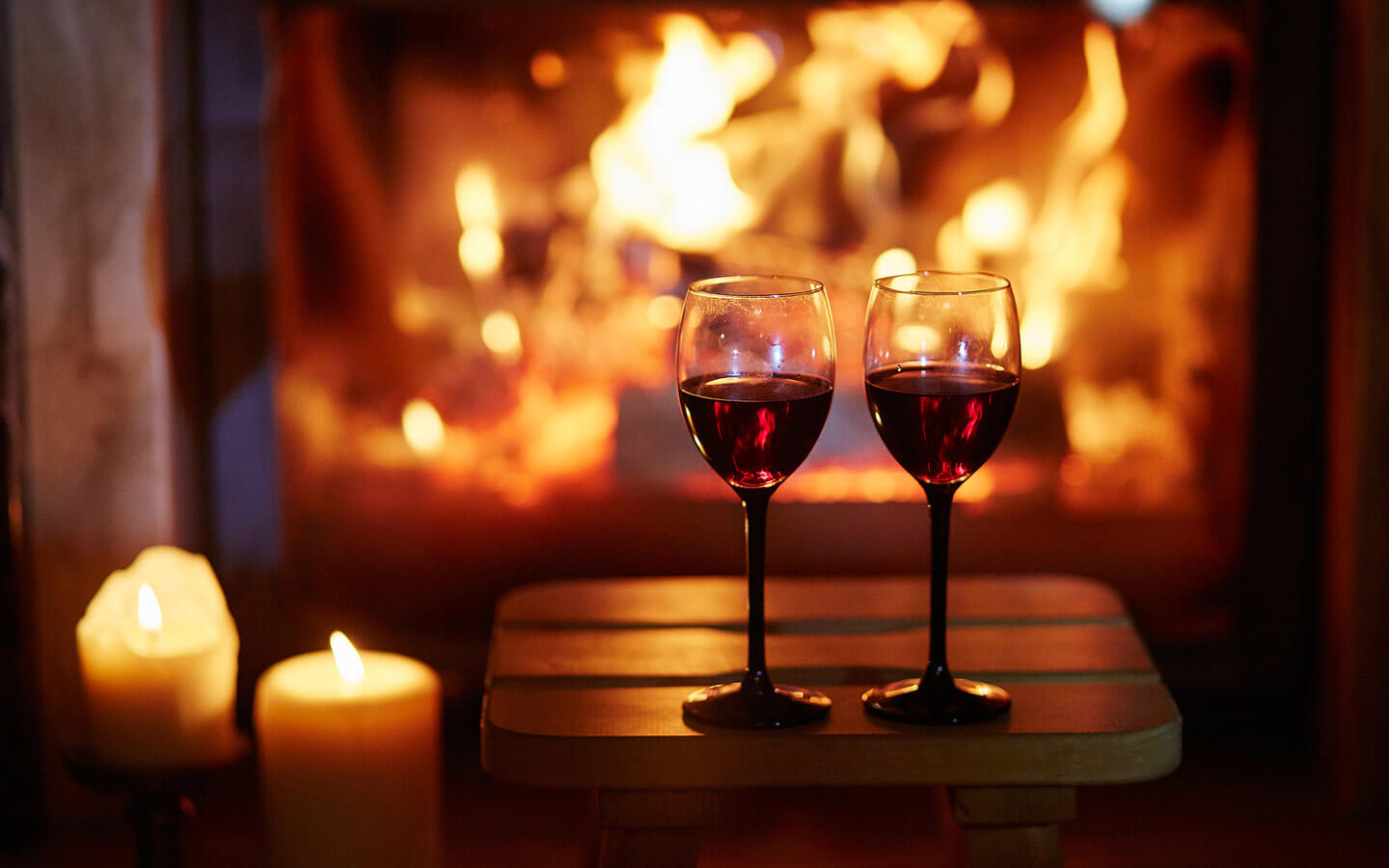 2 wine glasses in front of a fireplace with candles