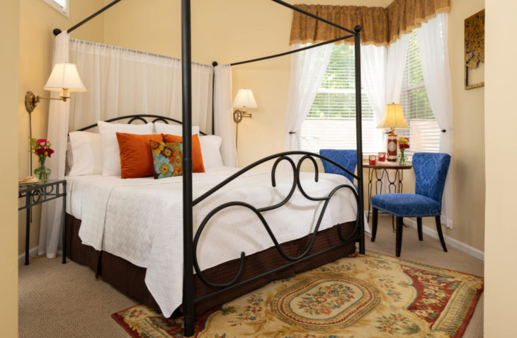 Room with a king size canopy bed side table and seating area