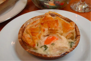 pot pie with carrots and green beens in brown bowl sitting on white plate dinner salad and crystal water goblet