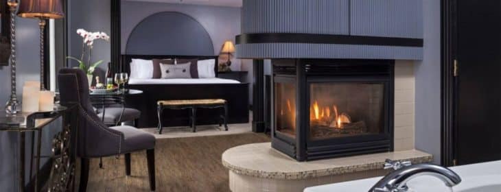 Deeply romantic grey and black guest room with modern touches, 3-sided fireplace and king-size bed.