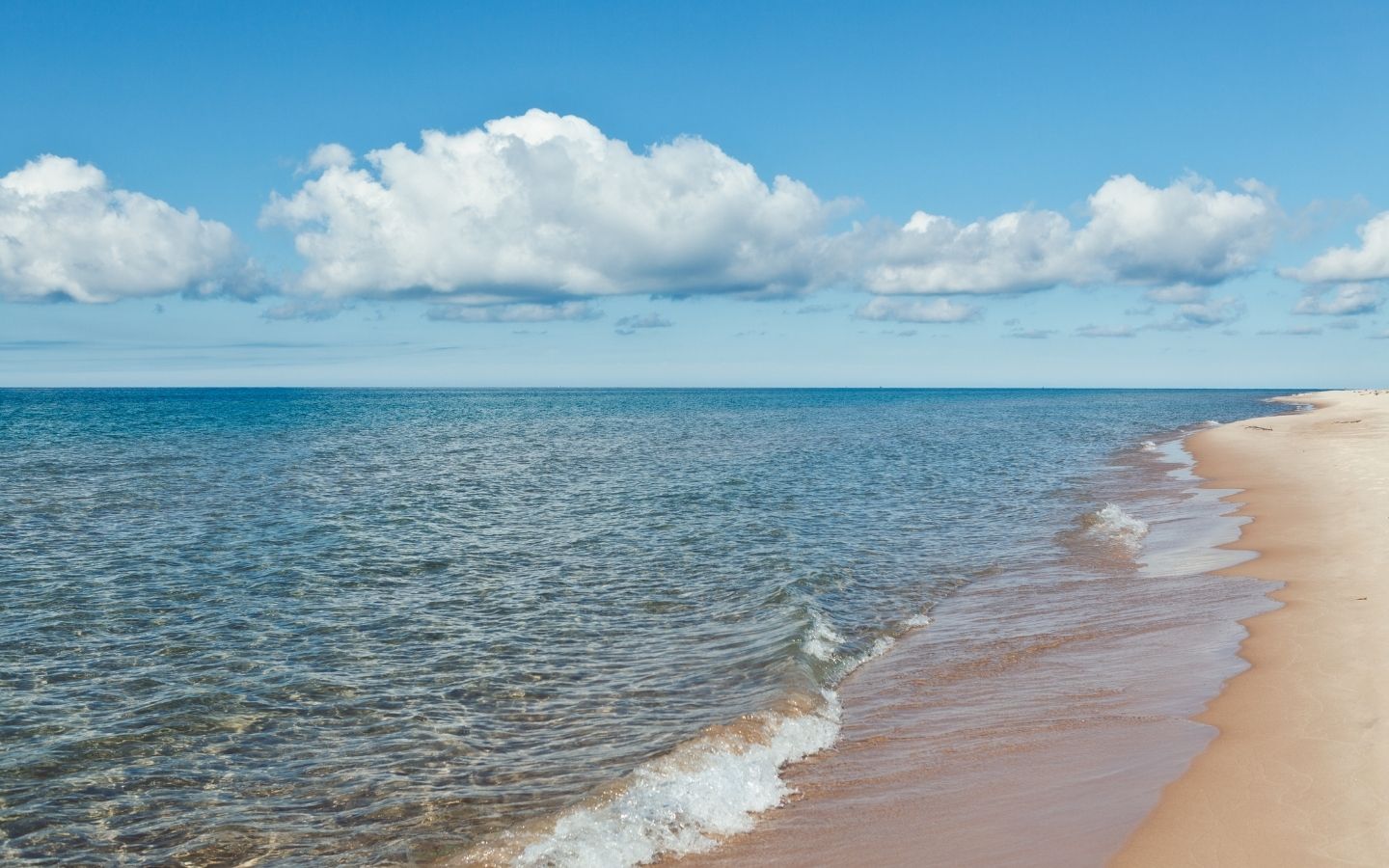 Beautiful view of Lake Michigan on a sunny day with puffy white clouds, a sandy beach, and gentle waves
