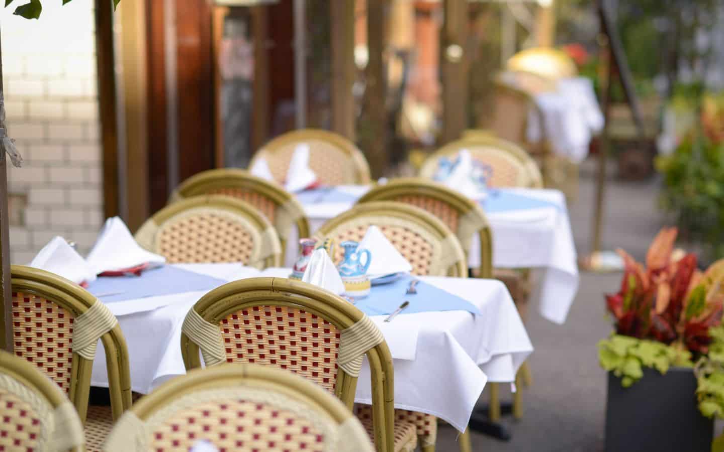 Cute wicker chairs and white linen topped tables on a sidewalk, set for dining