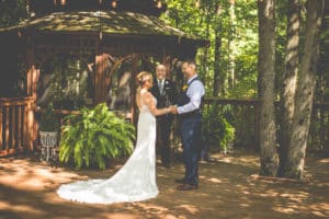 Groom and bride exchanging vows in front of a gazebo surrounded by trees