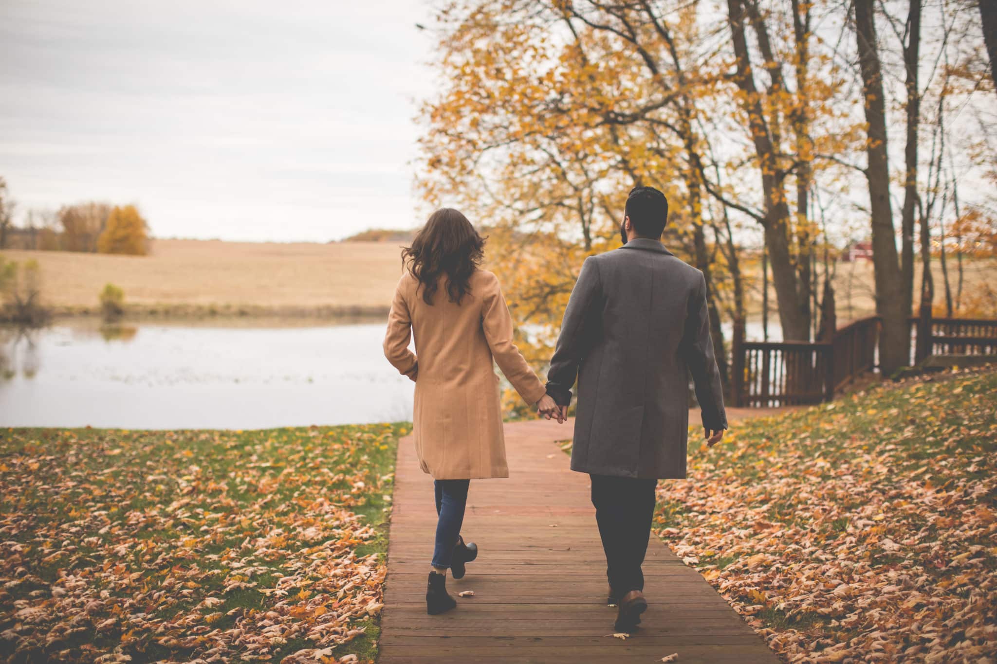 Couple walk hand in hand toward the pond with leaves falling